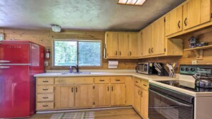 A kitchen with wooden cabinets, a red refrigerator, a microwave, a stove, and a window with a view of trees. - Cozy Florence Cabin, Proximity to Keyes Peak! (Florence)