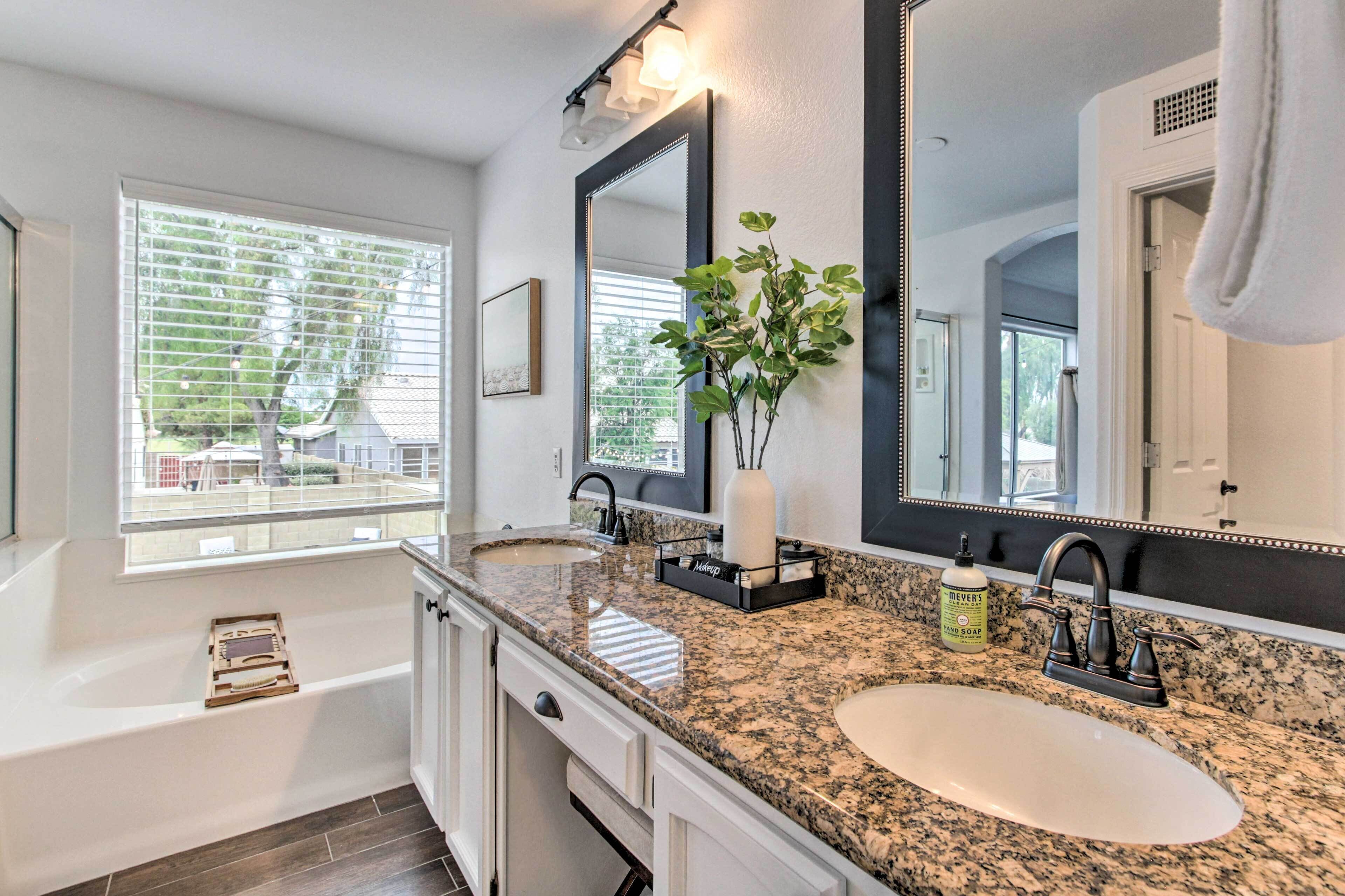 A modern bathroom with a double sink, a large mirror, a plant, and a bathtub.