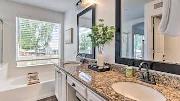 Un baño moderno con lavamanos doble, un espejo grande, una planta y una bañera.