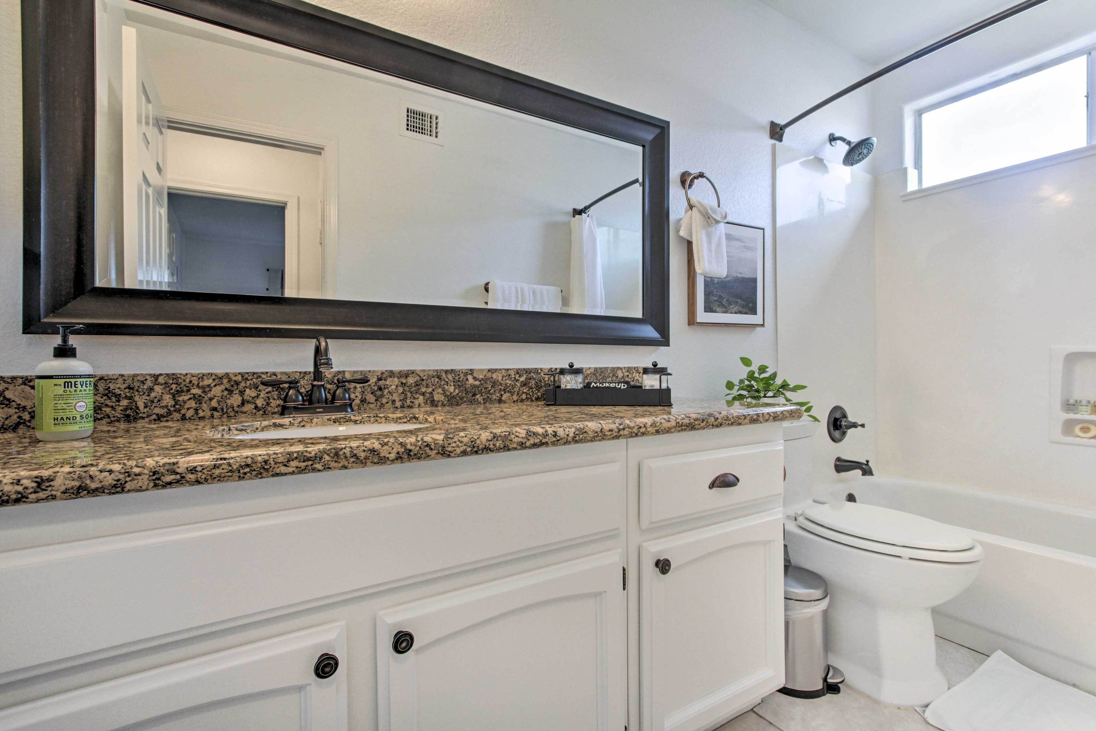 A bathroom with a granite countertop, white cabinetry, a large mirror, a toilet, and a shower.