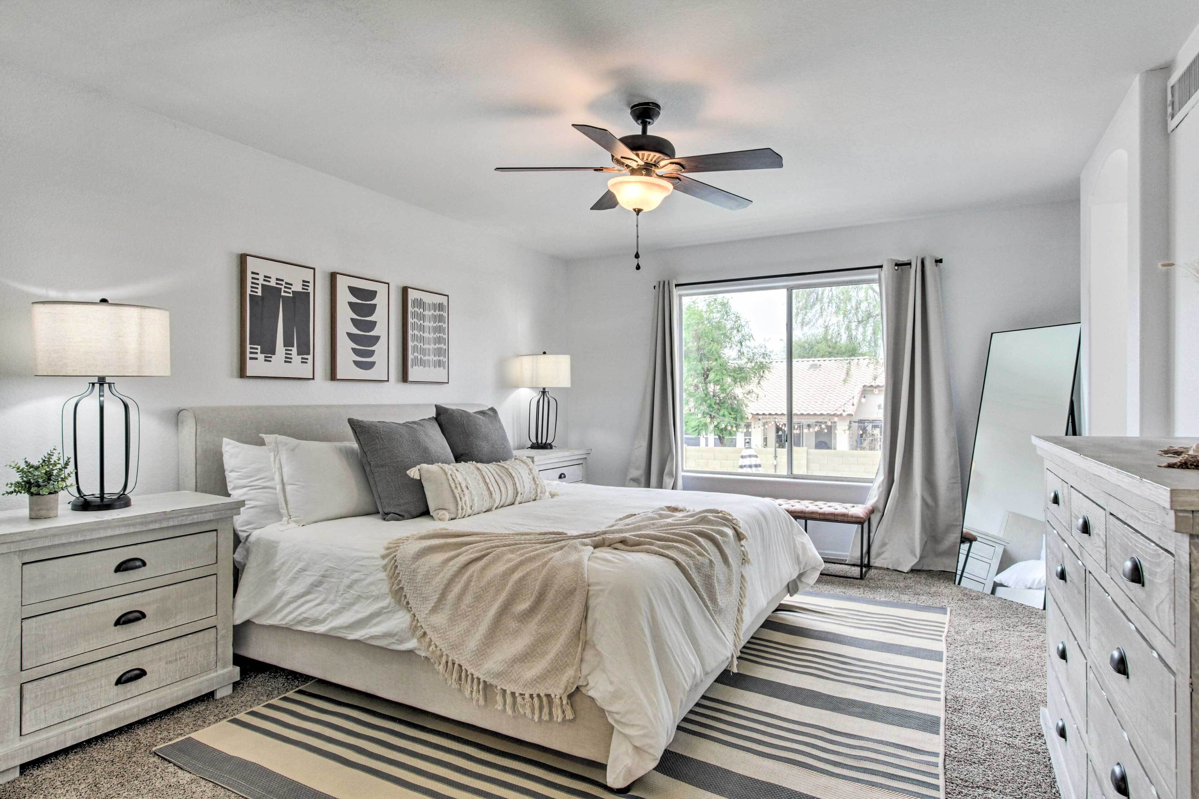 A bedroom with a bed, bedside tables, a ceiling fan, a window with curtains, and a dresser.