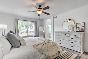 A bedroom with a bed, a dresser, a ceiling fan, a window, and a mirror. - Putting Green! Desert Group Getaway in Chandler (Chandler)