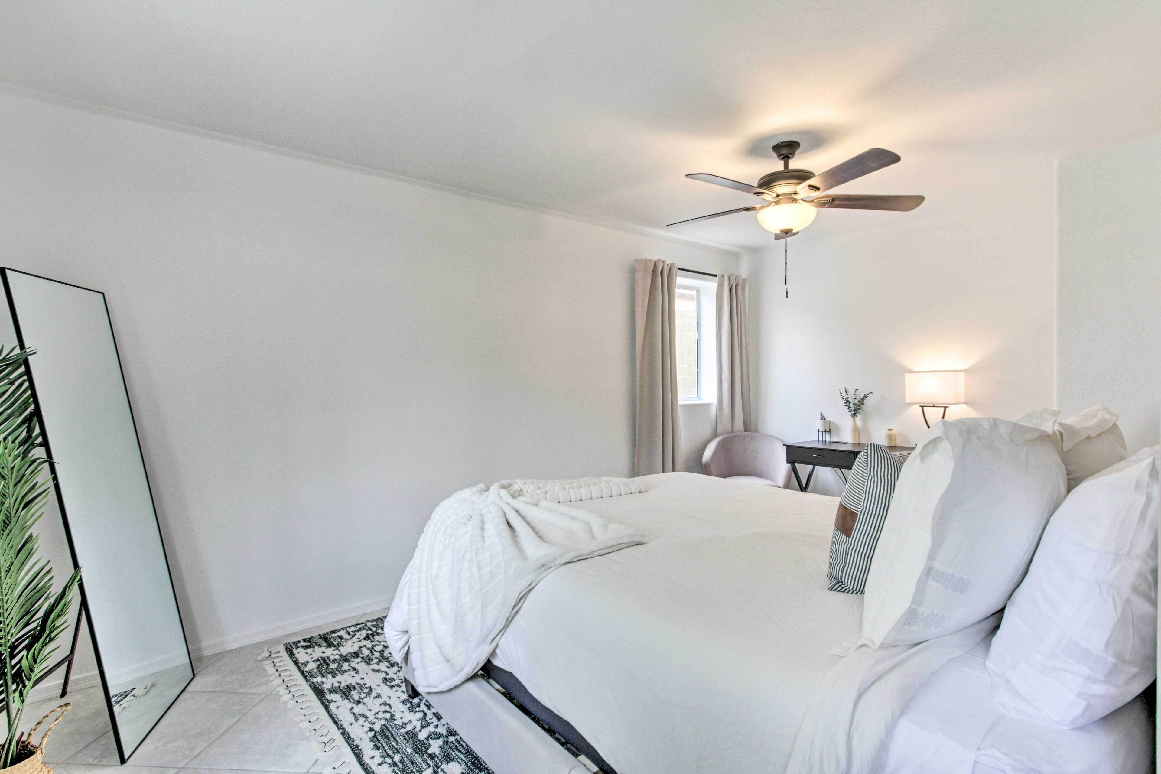 A bedroom with a bed, a ceiling fan, a nightstand, a lamp, and a window with curtains.