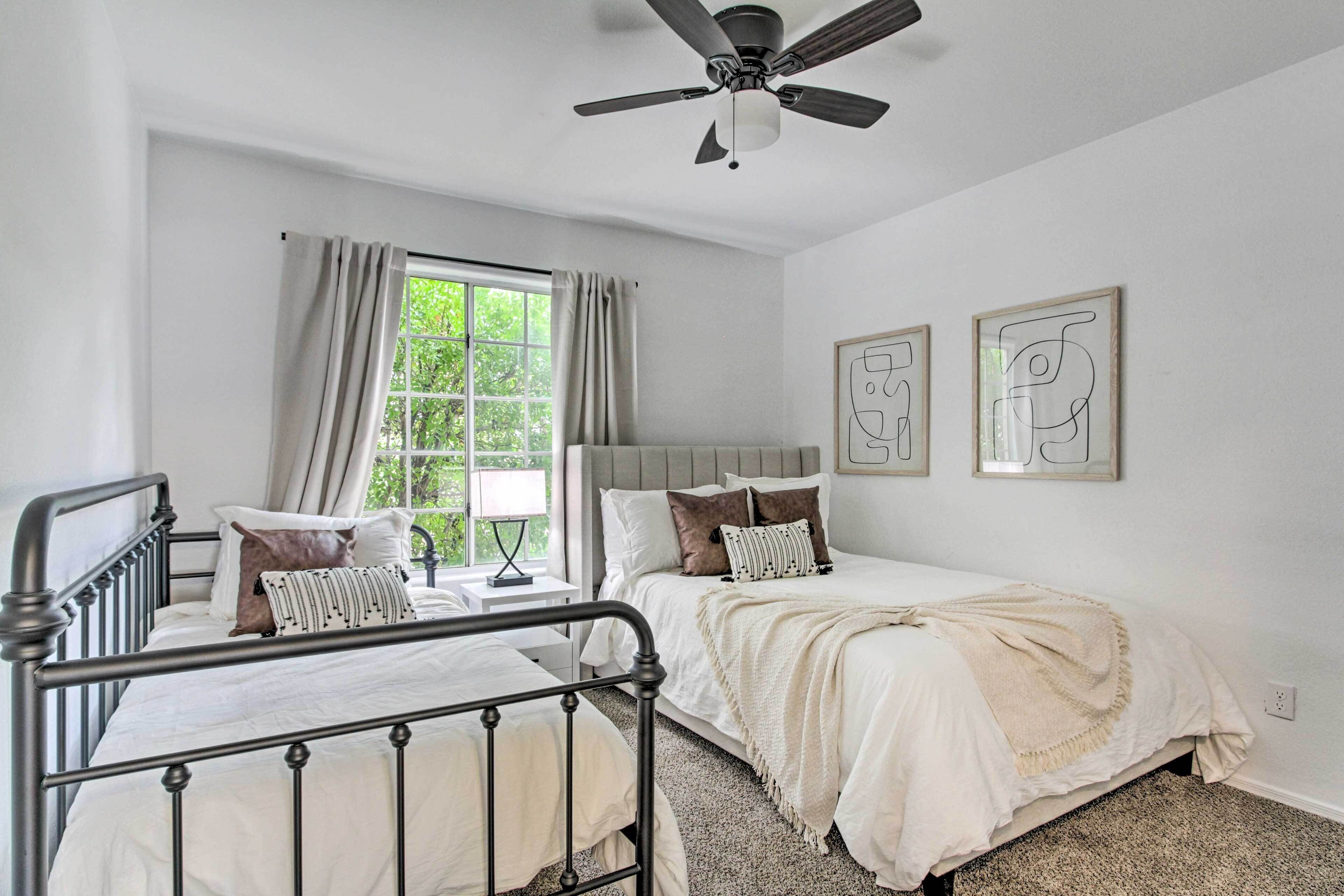 Ein Schlafzimmer mit zwei Betten, einem Deckenventilator, einem Fenster mit Vorhängen und zwei gerahmten Kunstwerken an der Wand.
