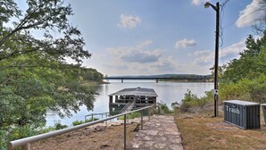 A stone pathway leading to a dock over water, with a trash bin and a lamp post nearby.