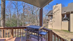 A covered deck with a barbecue grill, wooden deck, and a view of trees and a building in the background.