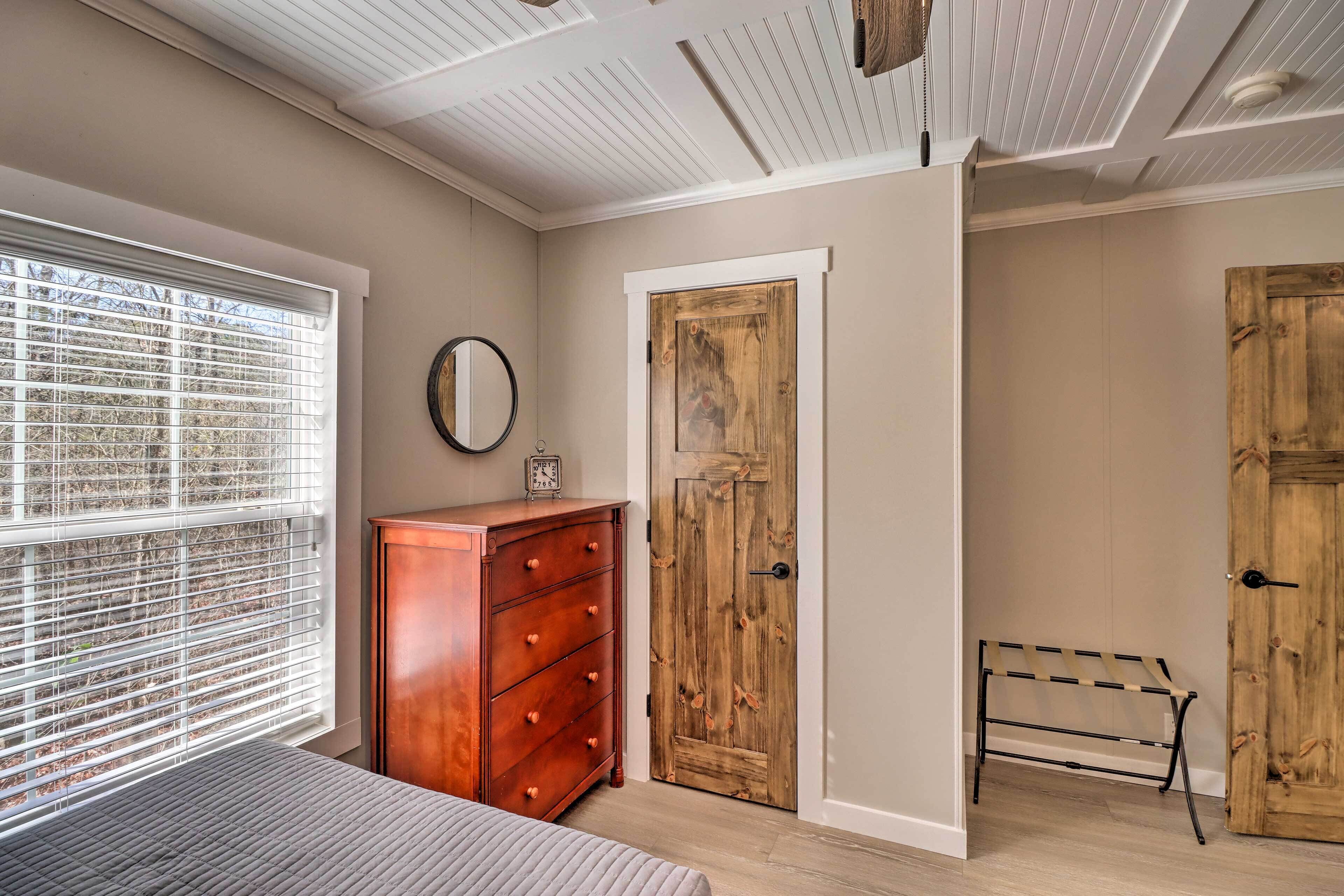 A bedroom with a bed, a wooden dresser, a wooden door, and a bench.
