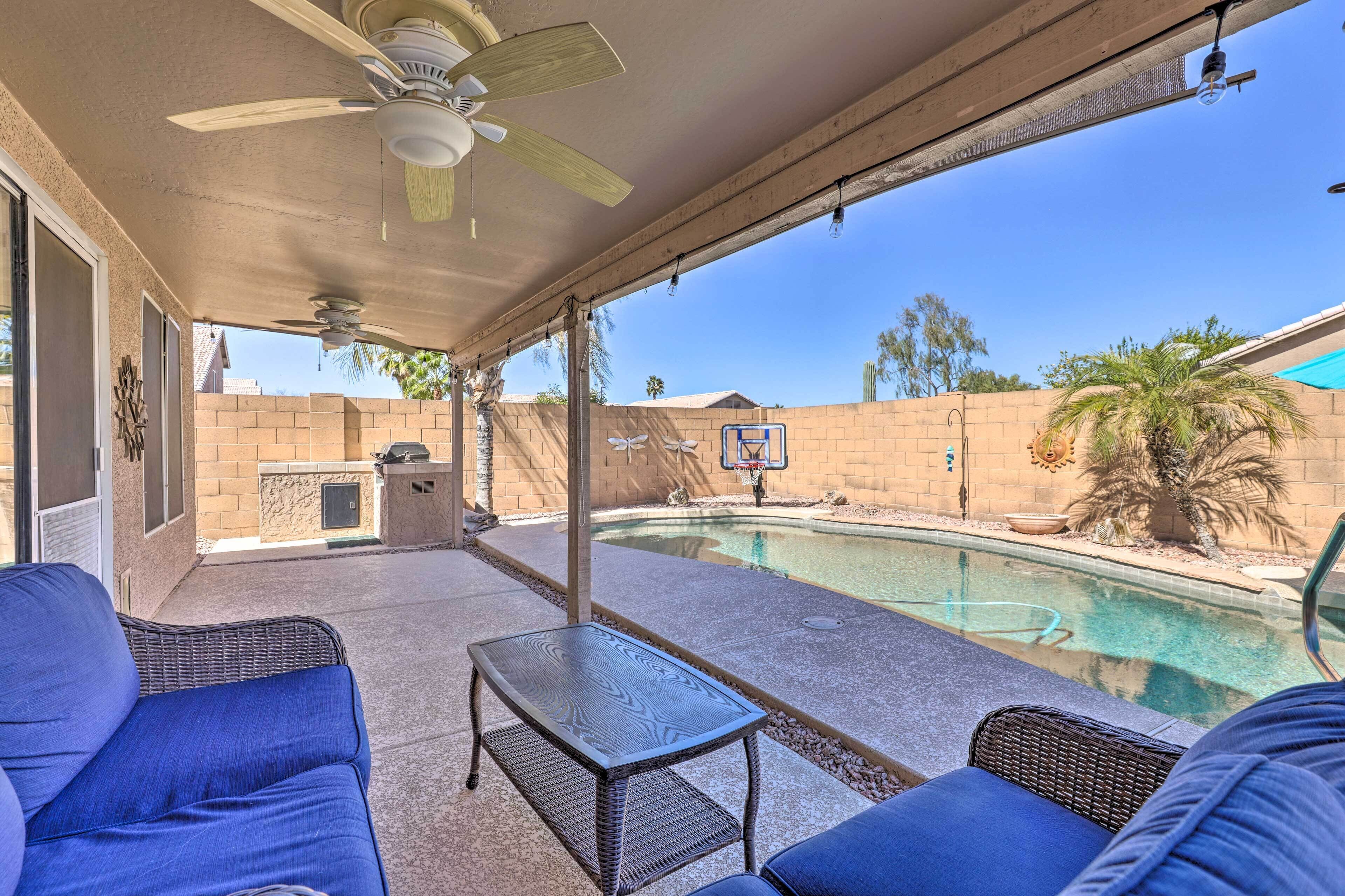 A covered patio with a pool, wicker furniture, and a ceiling fan.