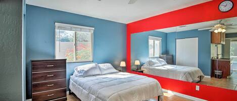 Une chambre à coucher avec un lit, une commode et un grand miroir qui reflète la pièce.