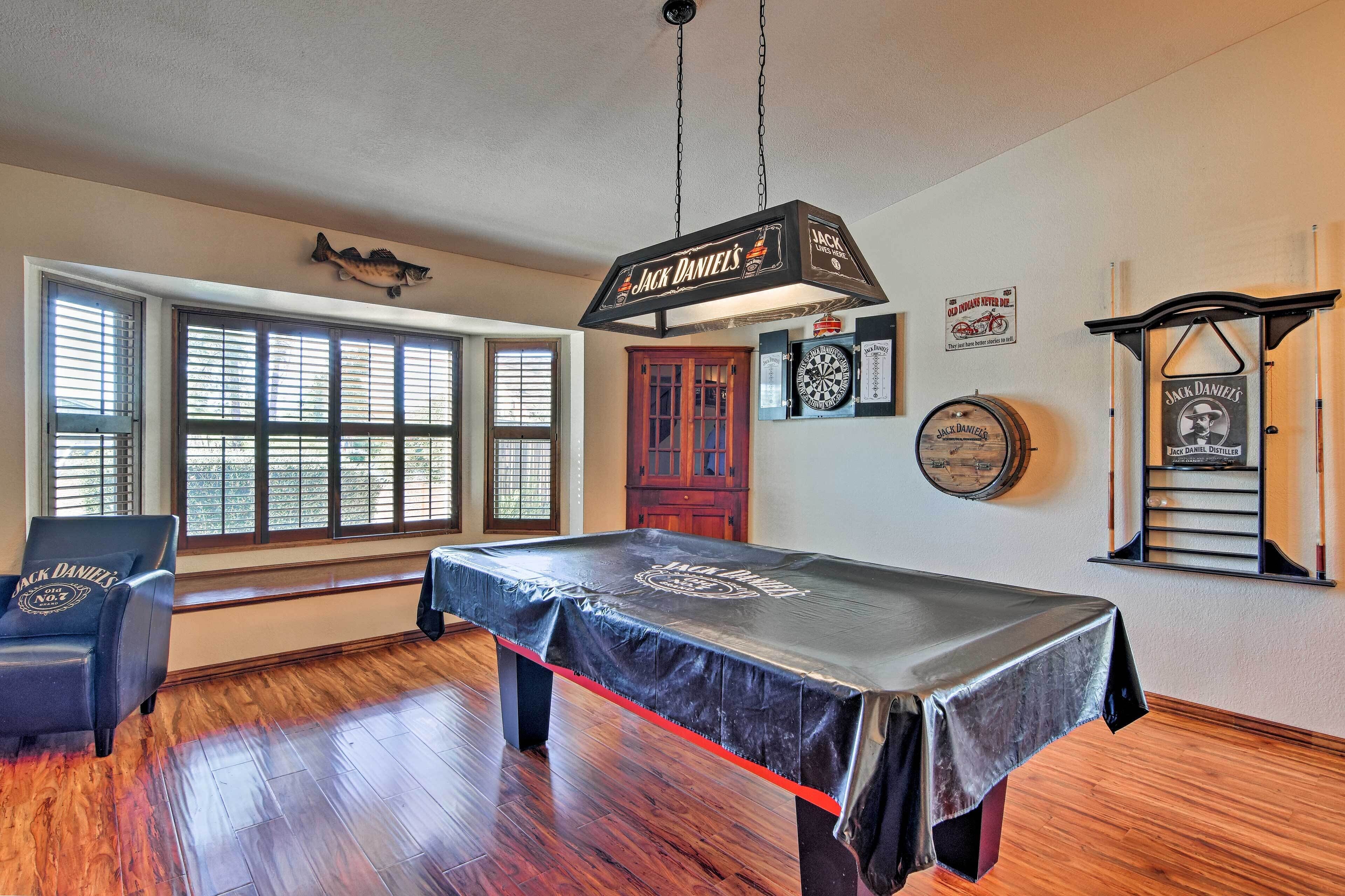 Una sala de billar con mesa de pool, un cartel de Jack Daniel's y un reloj en la pared.