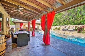 An outdoor pool area with a covered patio, red curtains, and a stone wall.