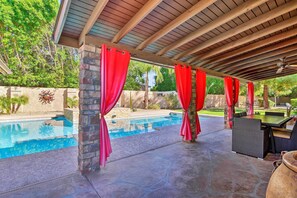 An outdoor pool area with a covered patio, stone walls, and red curtains.