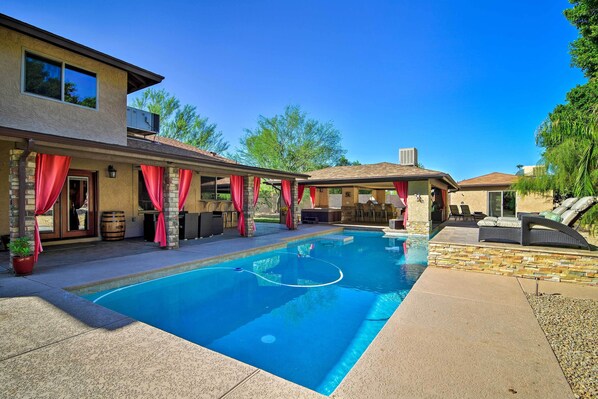 A backyard with a swimming pool, outdoor seating, and a covered patio area.