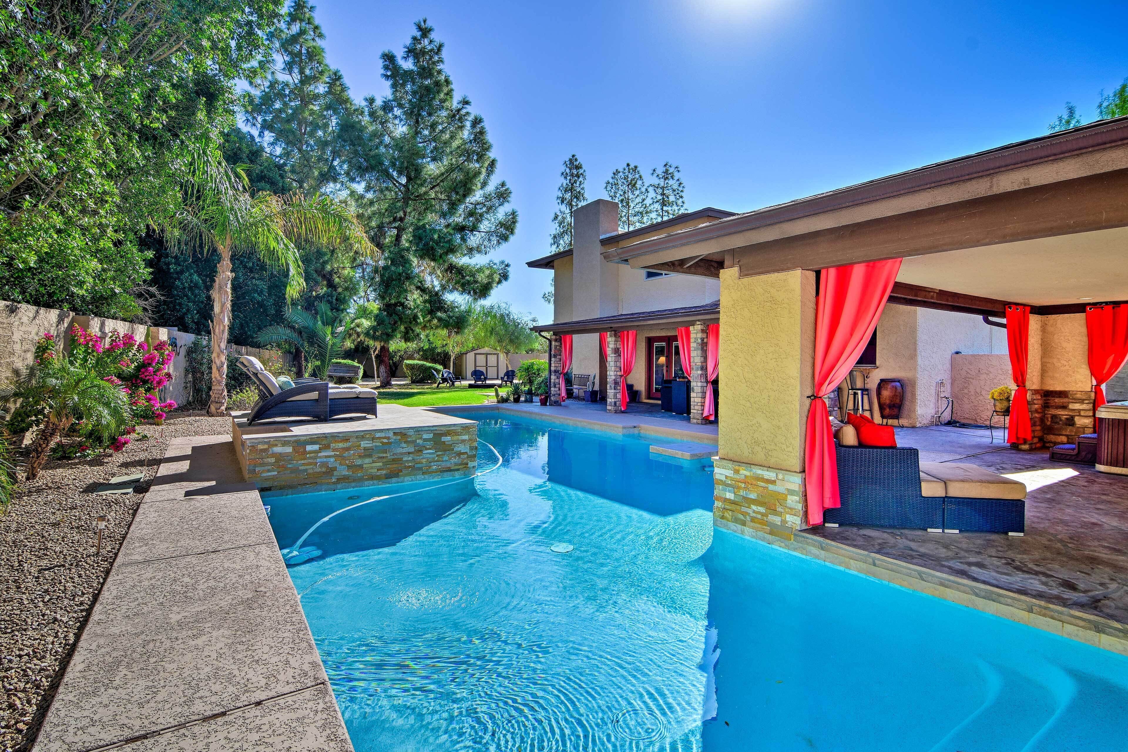 A swimming pool with a patio area, surrounded by trees and a stone wall.