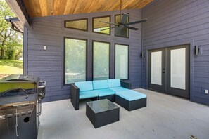 Un espace extérieur aménagé avec un coin salon abrité, comprenant un canapé bleu, une petite table et un barbecue.