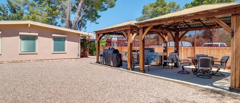 Un espace extérieur abrité, aménagé avec des tables et des chaises, un barbecue et un bâtiment doté de fenêtres.