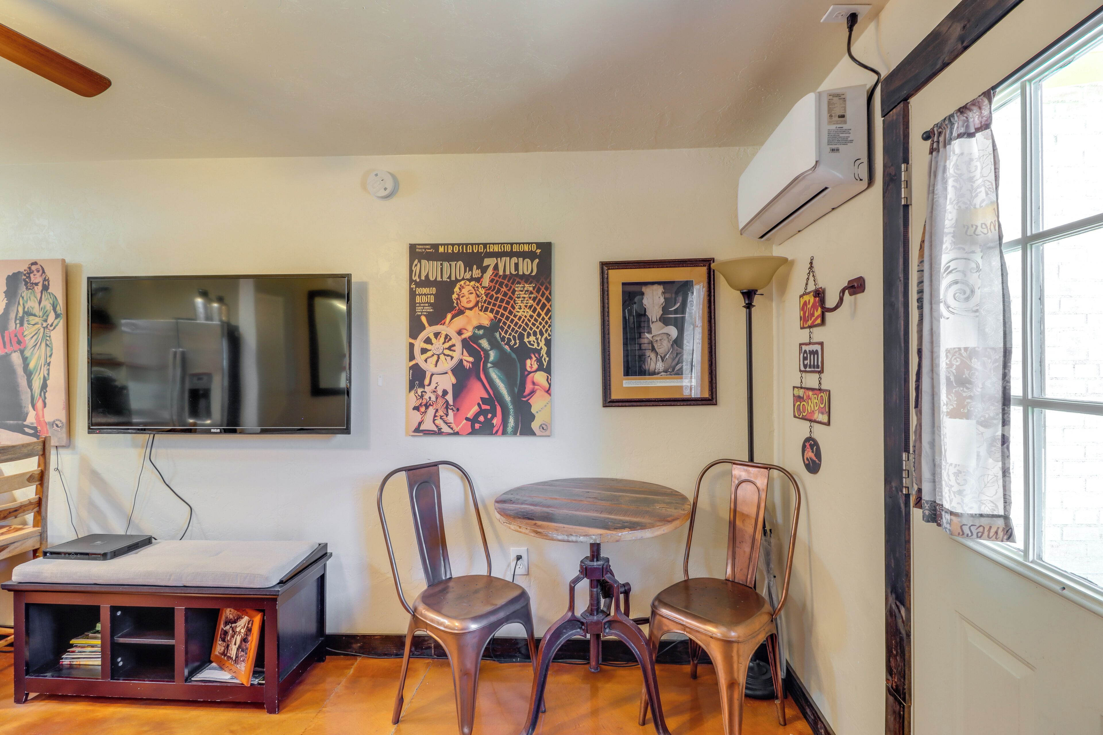 Een woonkamer met een televisie, twee stoelen, een bijzettafeltje en een boekenplank.
