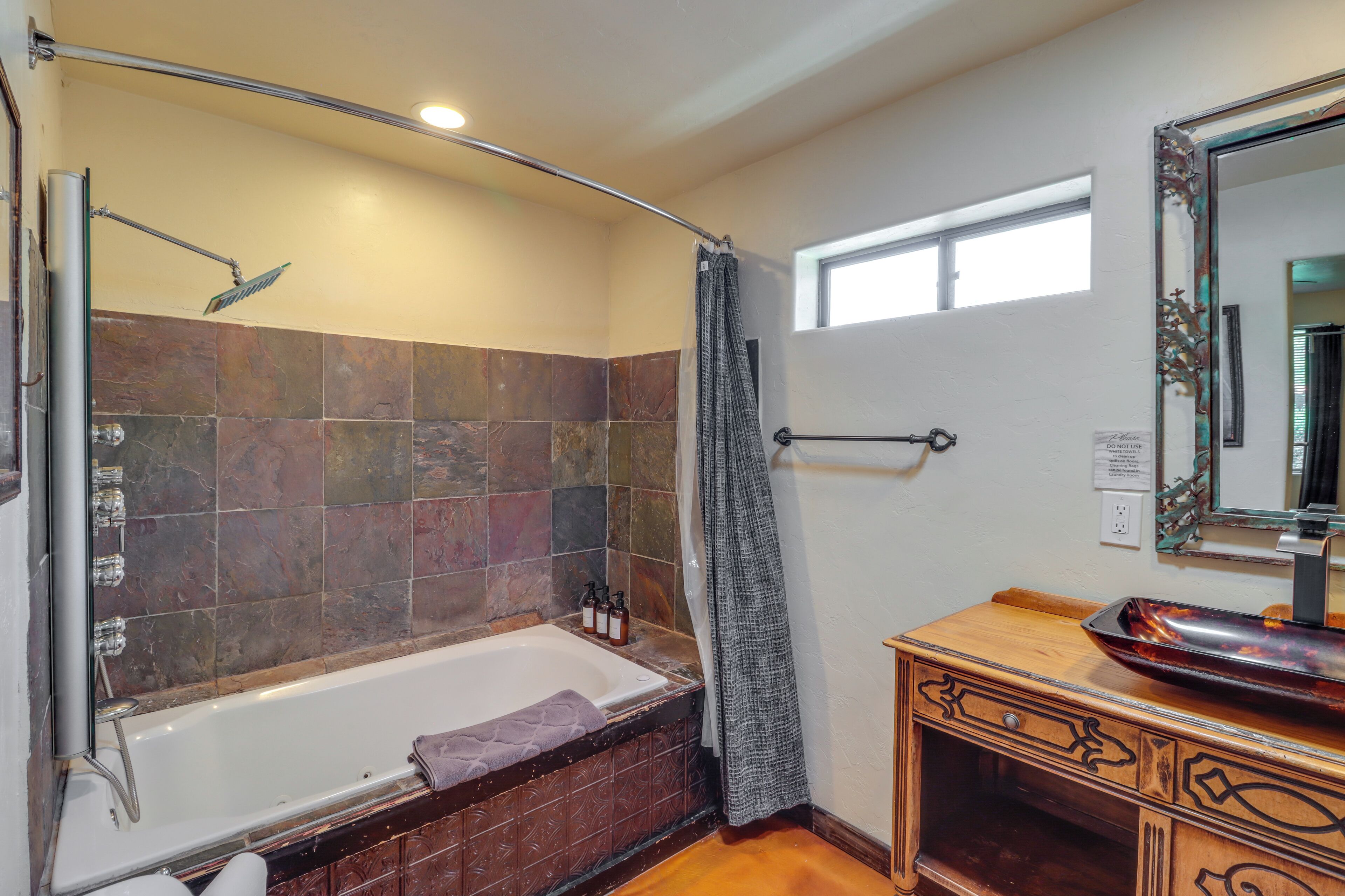 A bathroom with a bathtub, shower, vanity with a mirror, and a window.