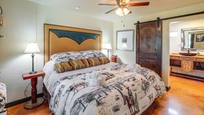 A bedroom with a large bed, a ceiling fan, a wooden door, and a bathroom with a sink and mirror.