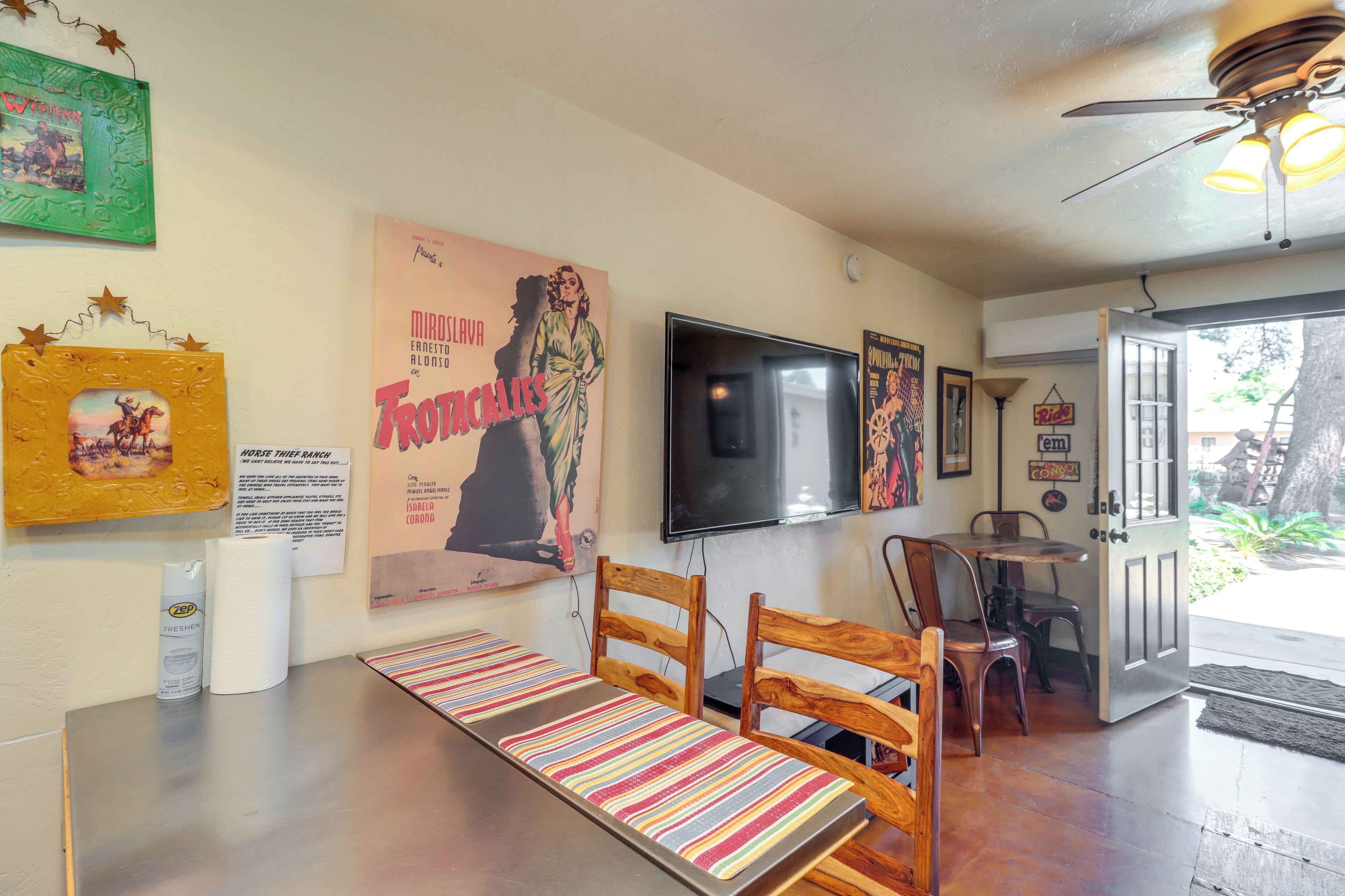 Une pièce avec un banc à rayures, des chaises en bois, un téléviseur et des œuvres d’art murales.