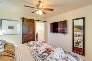 A hotel room with a bed, a ceiling fan, a TV, and a large mirror.