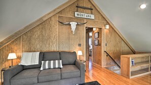 Ett rum i loftstil med ett sluttande tak av trä, en grå soffa, en svartvit matta och en träbänk.