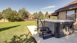 Un patio trasero con un jacuzzi, un pequeño conjunto de escalones que lo llevan y un césped bien cuidado.