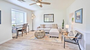 A modern living room with a ceiling fan, a sofa, a coffee table, and a desk with a chair. - Quaint Sedona Cottage w/ Backyard + Views! (Sedona)