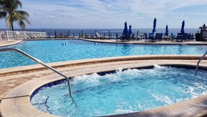 Un área de piscina con jacuzzi, sillones reclinables y sombrillas.