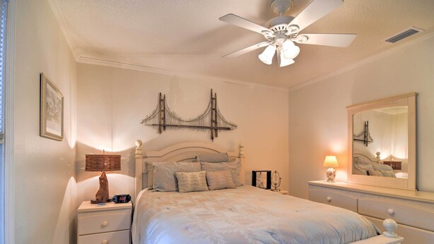Un dormitorio con cama, mesita de noche, cómoda, ventilador de techo y una obra de arte en la pared que representa un puente.