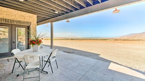 Une terrasse couverte avec une table et des chaises, une plante en pot et une vue sur un paysage désertique.