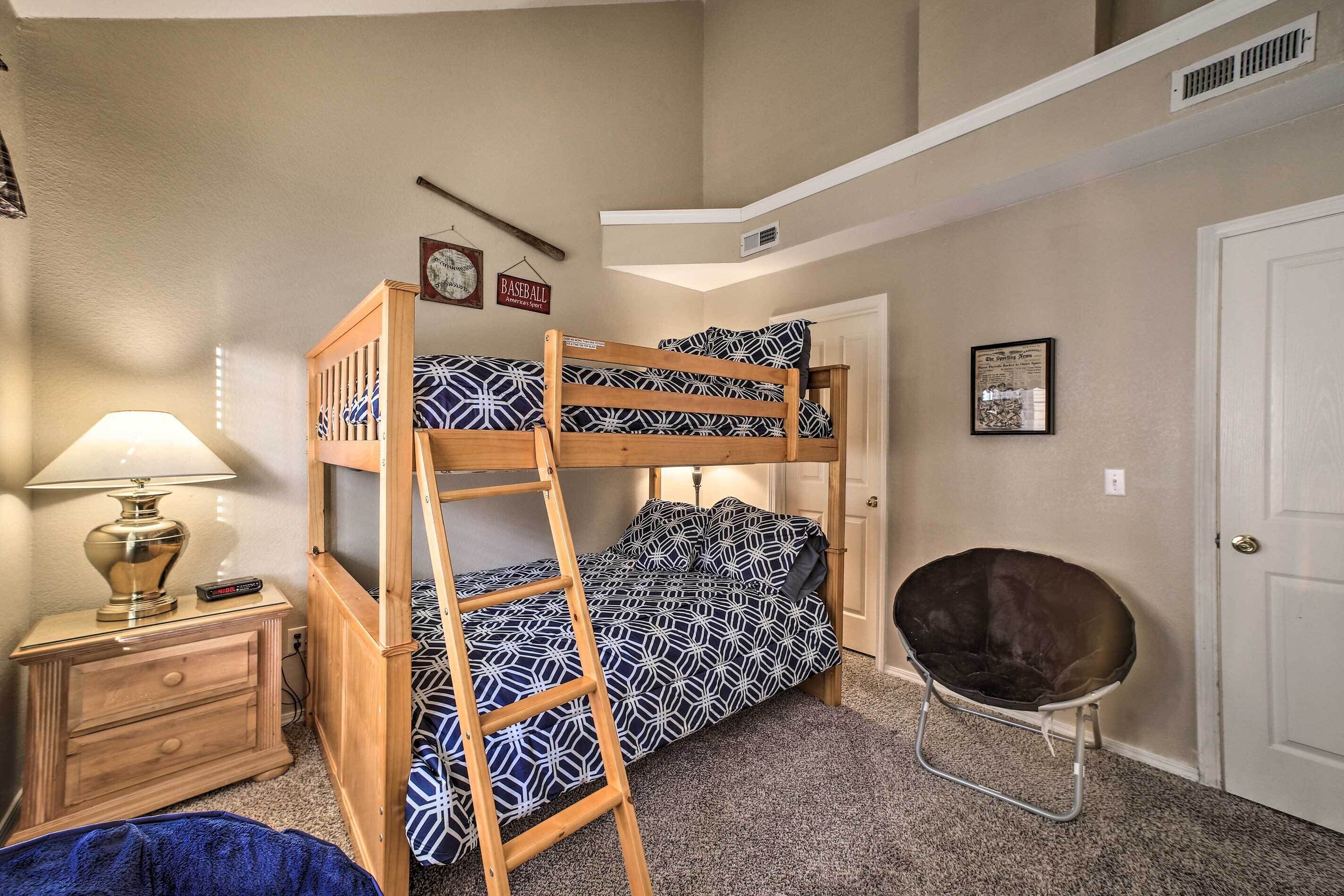 A bunk bed room with a ladder, a desk with a lamp, a chair, and a door.