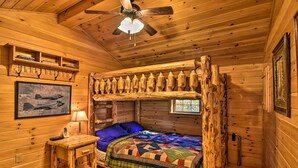 Una habitación tipo cabaña acogedora con una cama nido de madera, una mesita con lámpara y un ventilador de techo.