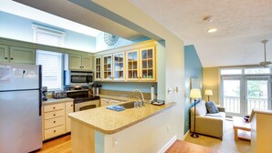 A kitchen with a central island, a dining area with a sofa and table, and a view of the outdoors. - Glen Arbor Vacation Rental w/ Views of Lake! (Glen Arbor)