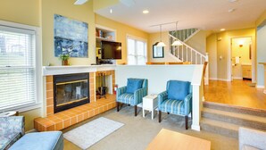 A living room with a fireplace, two armchairs, a coffee table, and a staircase leading to an upper level. - Glen Arbor Vacation Rental w/ Views of Lake! (Glen Arbor)