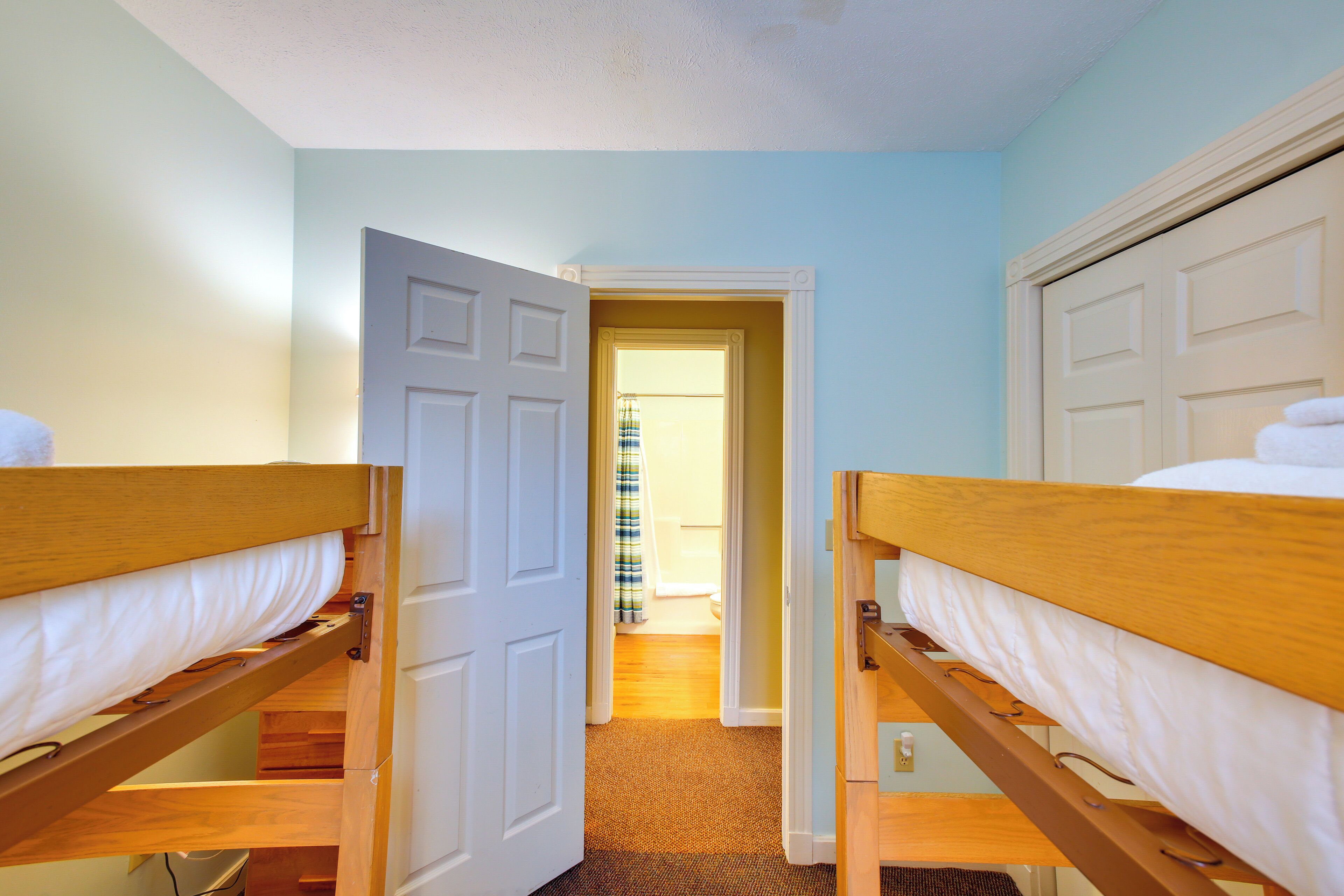 Een kamer met twee stapelbedden, een deur naar een andere kamer en een vloerbedekking.