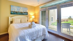 A hotel room with a bed, a painting of sailboats, a ceiling fan, and a view of the outdoors through a sliding glass door. - Glen Arbor Vacation Rental w/ Views of Lake! (Glen Arbor)