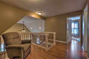 A spacious room with a wooden floor, a brown armchair, a white railing, and a ceiling fan. - Year-round Getaway < 1 Mi to Skiing + Waterpark! (McGaheysville)