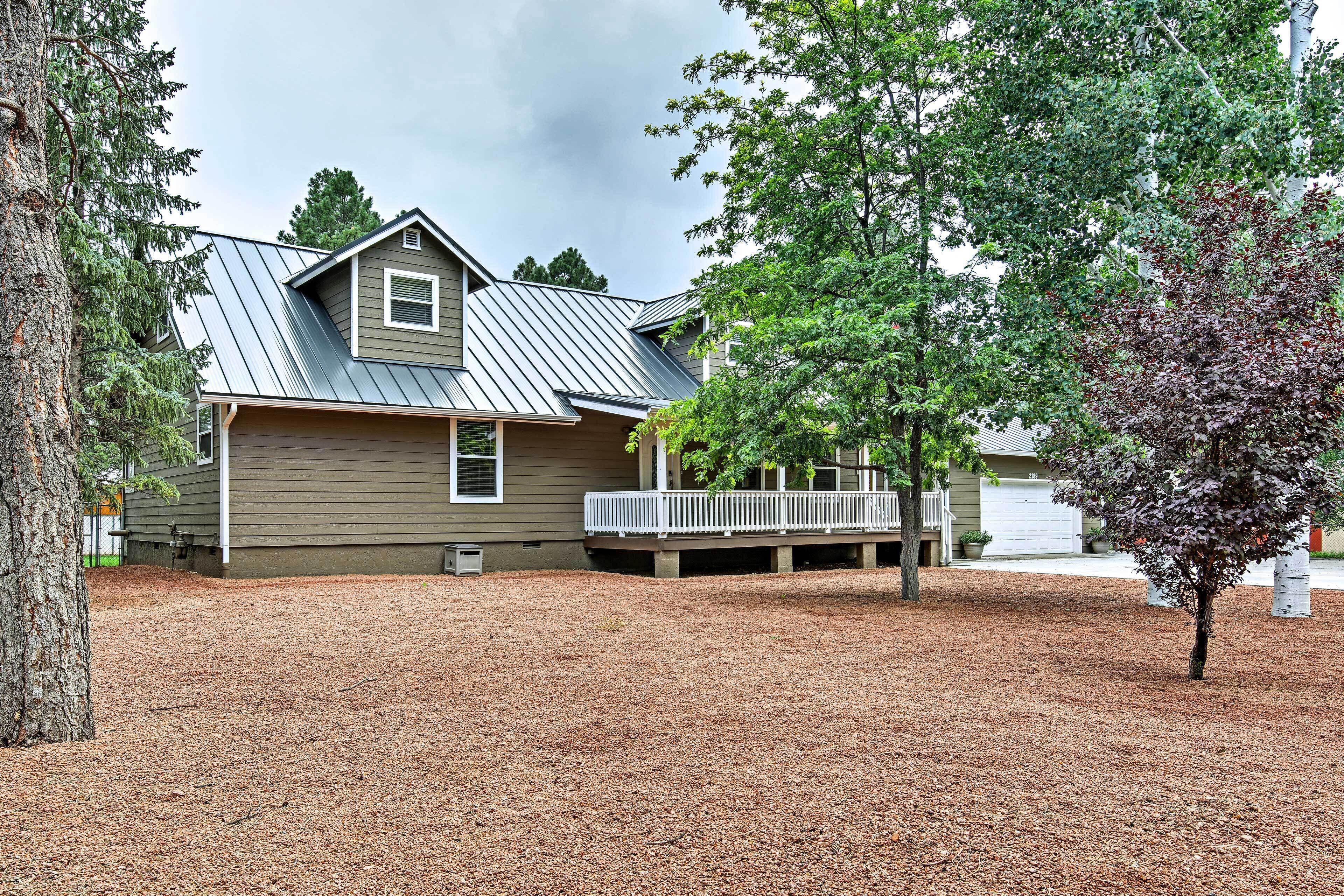 A two-story house with a metal roof, a covered porch, and a landscaped yard with mulch.