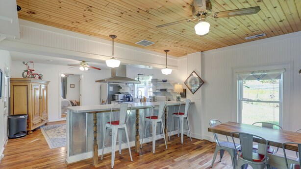 A spacious kitchen with wooden flooring, a central island, bar stools, and a dining table.