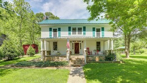 A two-story house with a green roof, a front porch, and a flag.
