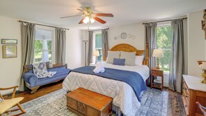 A bedroom with a large bed, a smaller sofa, a wooden bench, and a ceiling fan.