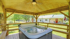 A wooden deck with a hot tub, a ceiling fan, and a view of a house in the background.