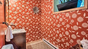 Un bagno con carta da parati a motivi floreali, un lavandino, uno specchio e una finestra con piante.