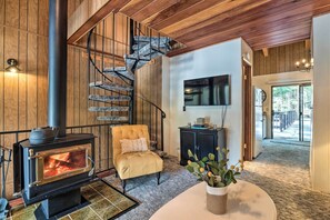 A cozy living room with a stone staircase, a fireplace, a comfortable armchair, and a view of the outdoors. - Pinecrest Retreat With Fireplace! (Pinecrest)