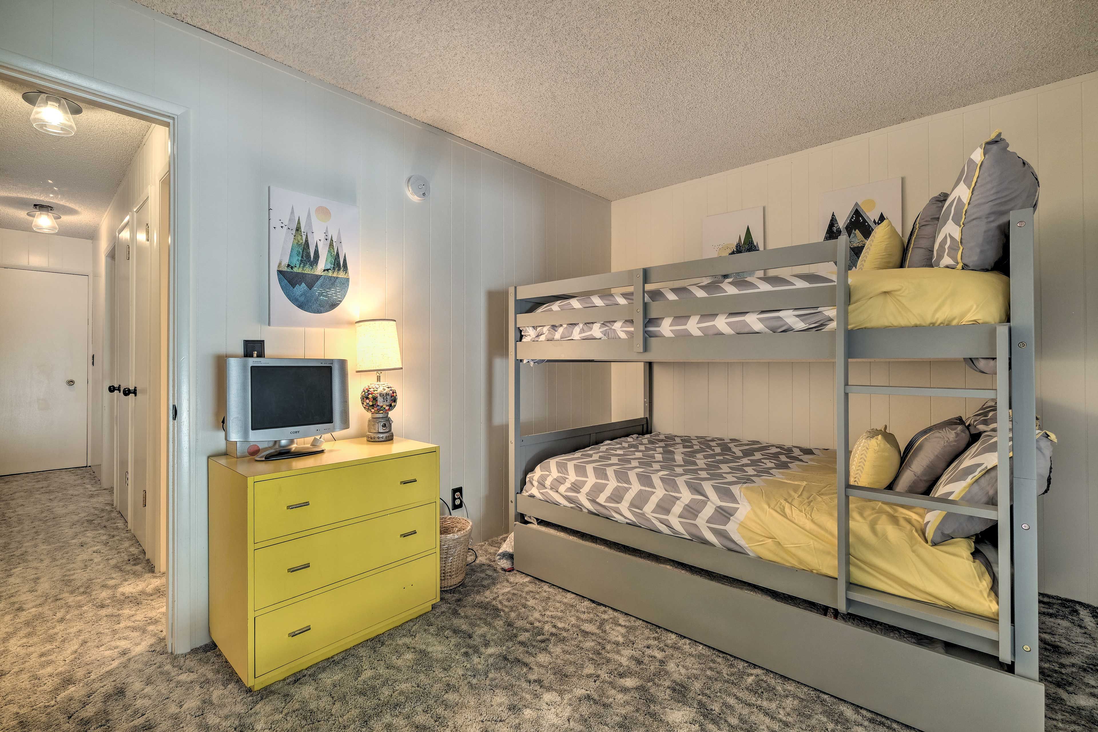 Un lit superposé avec une couvre-lit à motifs, une commode jaune avec des tiroirs et un téléviseur posé sur le dessus.