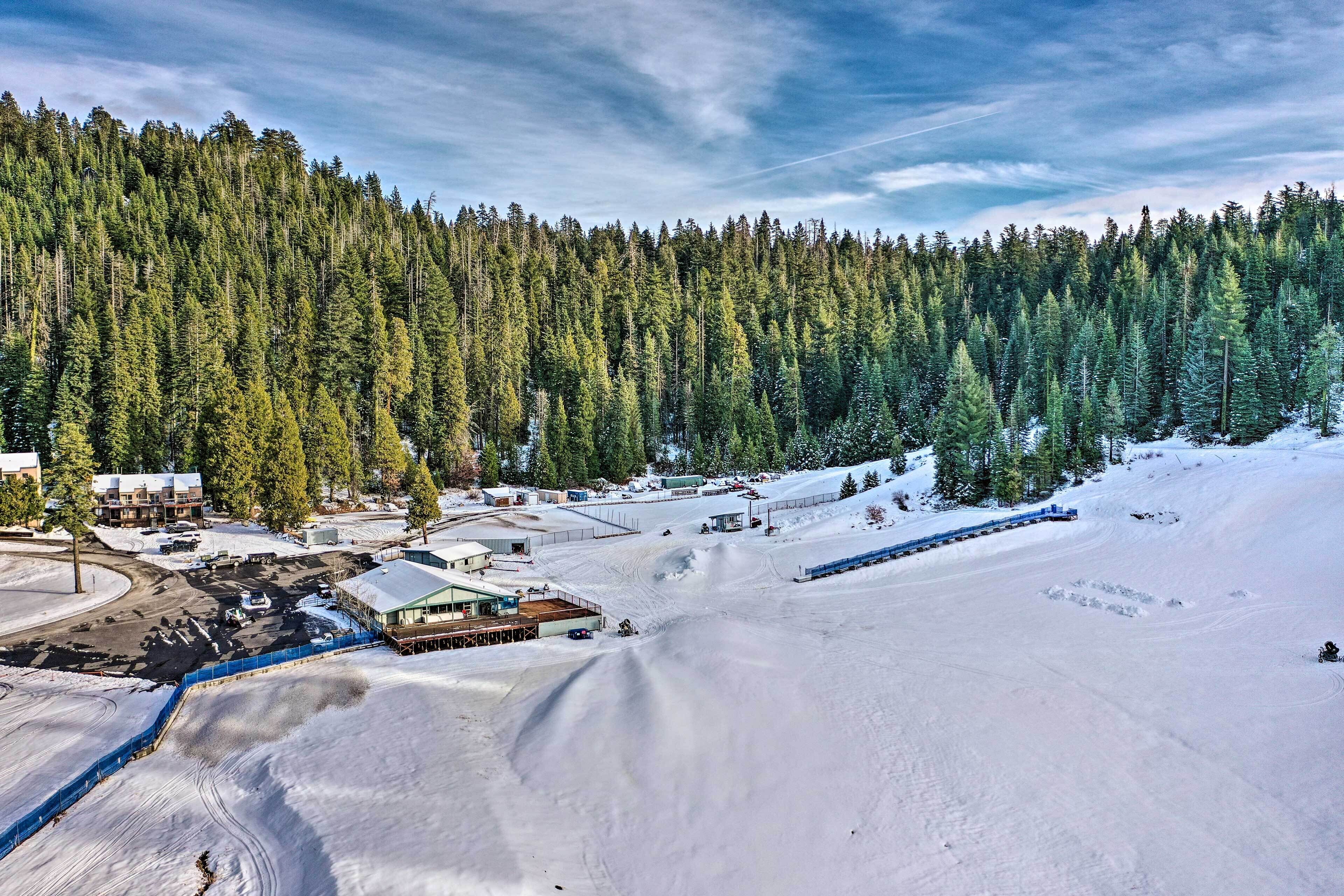 A snow-covered ski resort with a forested backdrop, ski lifts, and buildings.