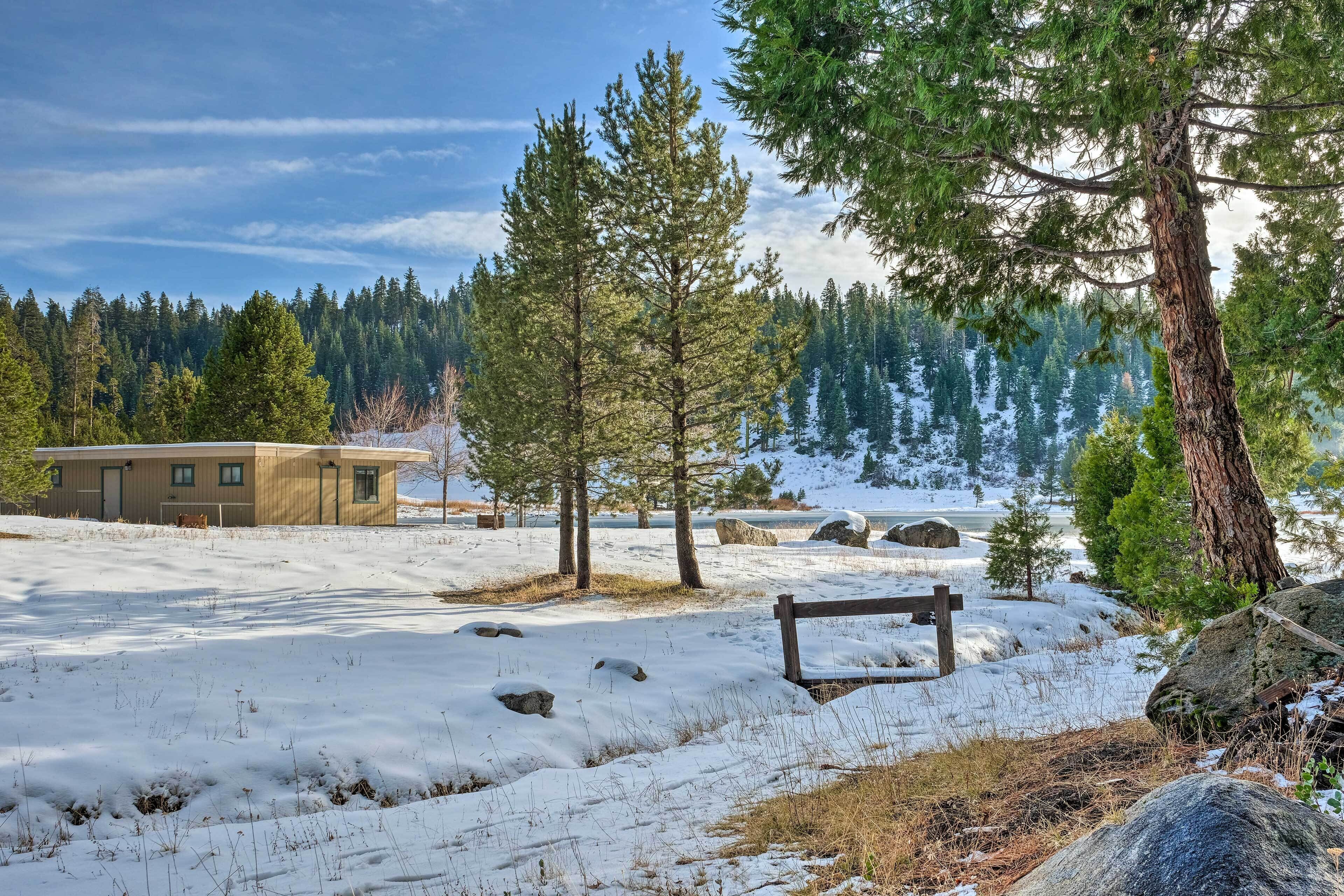 A cabin in a snowy forest with a wooden bench and a large rock.