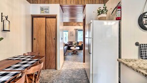 A cozy kitchen with a wooden ceiling, a white refrigerator, and a dining area with a checkered tablecloth.