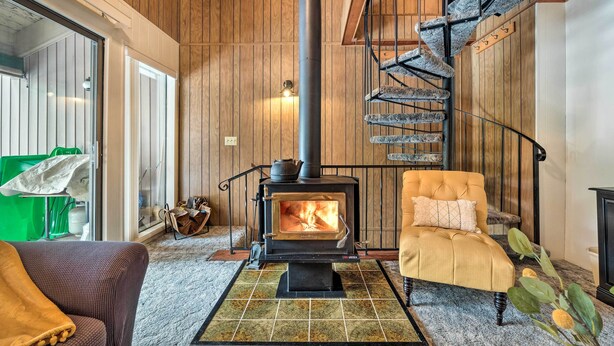 A cozy room with a wood-burning stove, a comfortable armchair, and a spiral staircase.